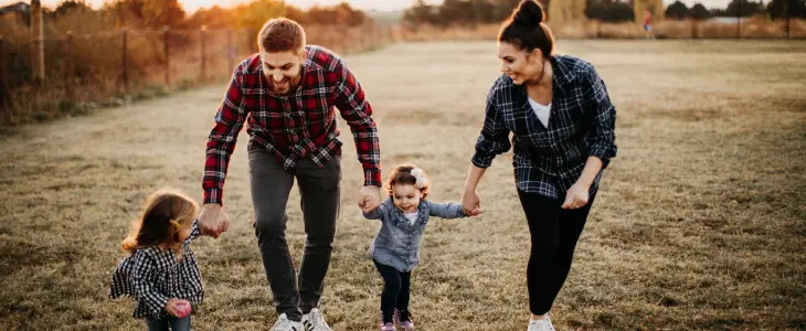 A family hold hands and laugh on a lawn