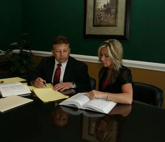Two professionals in formal attire reviewing legal documents at a desk.