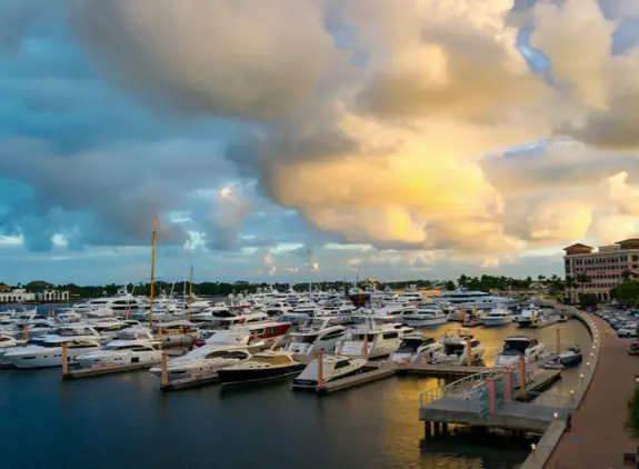 Luxury yachts docked at a marina under a colorful sunset sky.